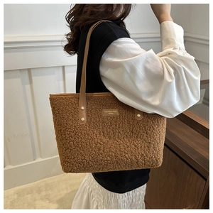 Close-up of brown plush tote bag with leather strap and metallic brand emblem