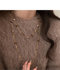 Détail du collier long double rang plaqué or 18k avec perles oeil de tigre sur pull marron