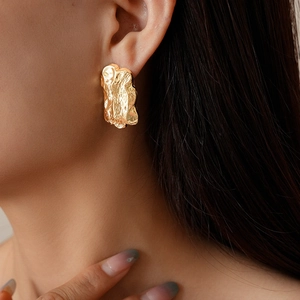 Macro side view of gold irregular textured earrings with molten lava design on model