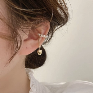 Dettaglio dell'ear cuff dorato con perle bianche e nappa con pendente a forma di cuore
