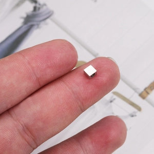 Polished 4mm stainless steel cube bead with 1.8mm hole shown on fingertip for scale