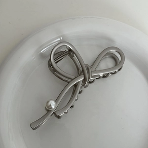 Detail view of silver metal bow hair claw clip with a single pearl on ceramic tray