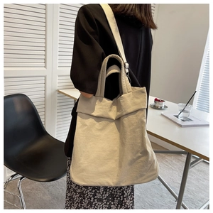 Detailed model view of an off-white canvas tote bag with shoulder strap and handles