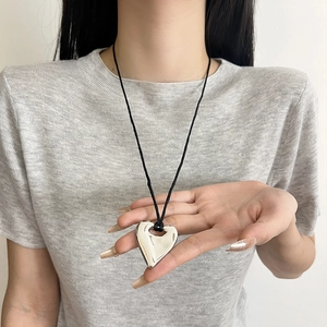 Polished silver heart pendant necklace with black cord cord shown in hand for scale