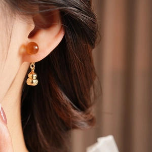 Detail of vintage gourd pendant earring with a reddish bead worn on a model's ear