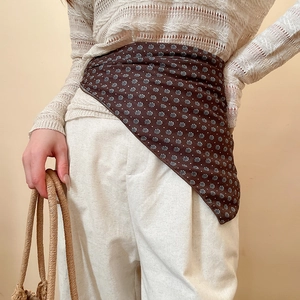 Detail of a dark brown floral scarf with blue print worn as a decorative waist belt