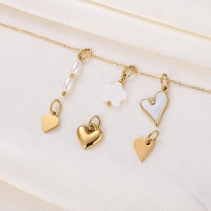 Detail of vintage heart and pearl charms on gold necklace over beige silk fabric