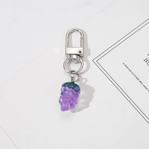 Close-up of purple resin grape keychain with silver metal carabiner on a white surface