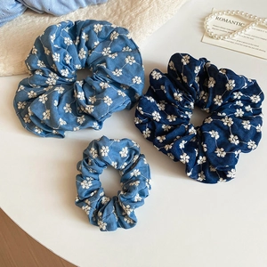 Detail showing blue denim fabric texture and white floral embroidery on hair scrunchies