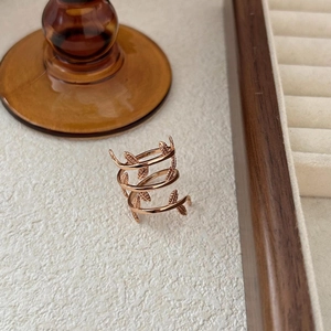 Close-up of rose gold leaf wrap ring detail on a wooden display tray with soft lighting