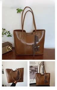 Detail view of brown leather tote bag with vertical white stitching and cute charms