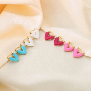 Detailed view of colorful heart-shaped enamel hoop earrings on beige satin fabric
