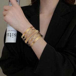 Detailed close-up of five-piece 18K gold layered bracelets worn by a model in black suit
