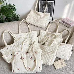 Detail of white quilted tote bags with floral embroidery and red bow accents
