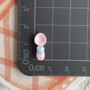 Detailed view of pink resin mini spoon charm with blue heart on a measurement mat