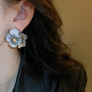 Close-up of vintage flower earrings with pearls and blue zircons worn by a model