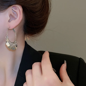 Close-up of silver multi-layered sequin tassel hoop earrings worn with a black blazer