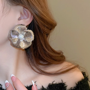 Detailed view of oversized metal flower earring with pearl center on model