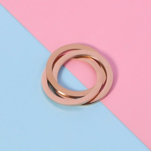 Macro detail of rose gold triple interlocking rings on a pink and blue background