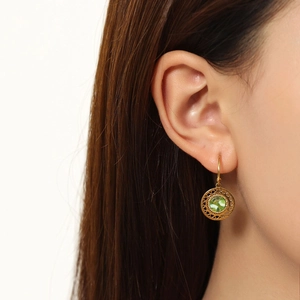Detailed close-up of a model wearing a gold hollow-out earring with a green gemstone inlay