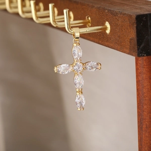 Dettaglio macro del ciondolo a croce dorata con zirconi marquise su un supporto di legno