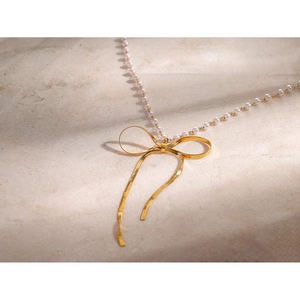 Detail of 18k gold butterfly pendant on white pearl necklace over beige stone