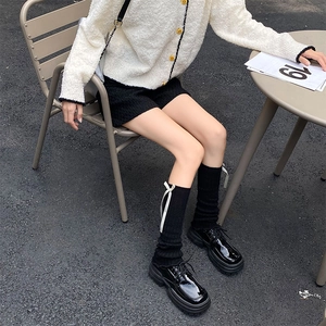 Detail of black knit leg warmers with white bows styled with glossy platform shoes