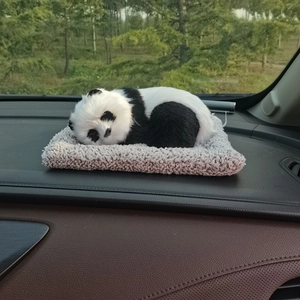Detailed close-up of a realistic panda plush doll sitting on a grey car dashboard mat
