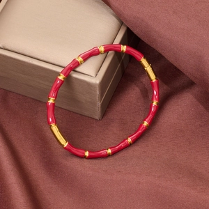 Close-up of red enamel and gold bamboo-style stainless steel bracelet on red silk fabric