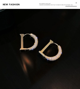 Macro shot of gold D-letter earrings with shimmering white zircon stones on black background