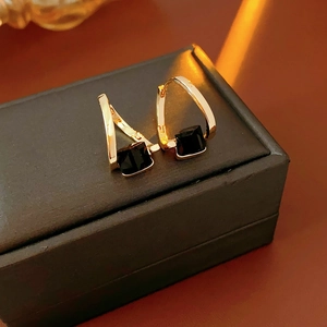 Close-up of gold square earrings with black stones on a black jewelry box