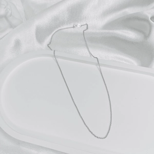 Detail of minimalist silver-plated chain necklace on elegant white silk tray