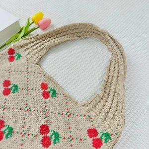Detailed close-up of beige knitted tote bag with red cherry and green plaid patterns