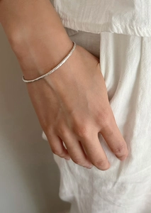 Minimalist silver textured bangle with a unique hammered finish on a model's wrist
