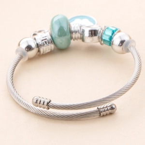 Detail of silver plated charm bracelet with light green glass beads and blue cloud pendant