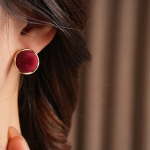 Close-up of deep red velvet geometric stud earrings with gold trim worn by model