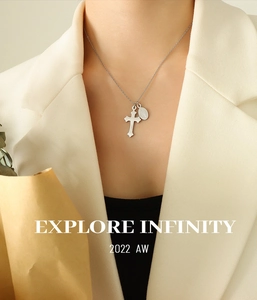 Détail du collier à pendentif croix d'argent et médaille sur un blazer beige chic