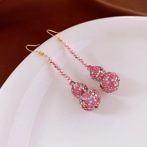 Detail of pink crystal gourd tassel earrings with iridescent rhinestones on a white plate