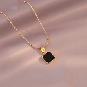 Minimalist black square pendant necklace with gold bead chain on silk background