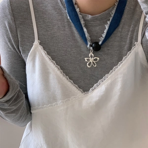 Detail of floral pendant necklace with denim ribbon and black bead on female model