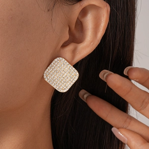 Close-up of elegant square gold stud earrings with pavé rhinestones on model's ear