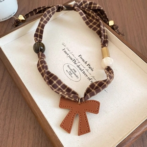 Close-up of vintage brown plaid fabric choker with leather bow and retro beads