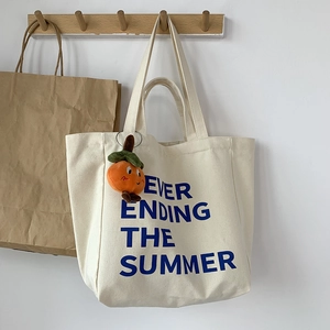 Detail of canvas tote bag with blue text and a cute orange persimmon plush charm