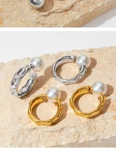 Macro shot of silver and gold C-shaped stainless steel pearl earrings on a stone base