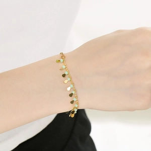 Close-up of elegant gold chain bracelet with green beads and leaf charms on wrist