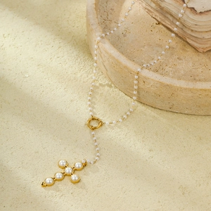 Cross pendant necklace with white pearls on a gold chain, displayed on a stone platform