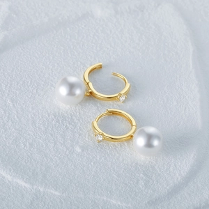Detail of golden pearl hoop earrings with zirconia on white marble texture background