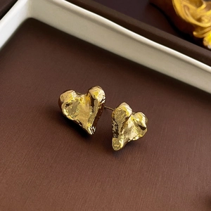 Macro shot of gold heart earrings with irregular lava texture on dark display