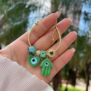 Close-up of gold chain bracelet with green enamel charms and hamsa evil eye pendants