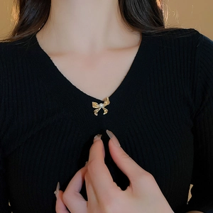 Detail of a gold-plated bow brooch with a pearl center on a black knitted sweater